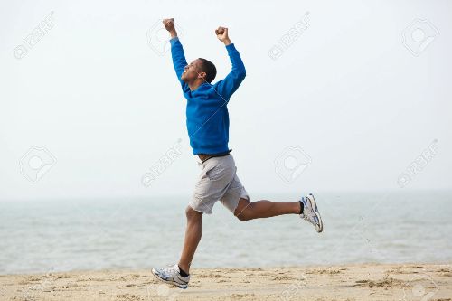 African american man running with hands raised at the beach