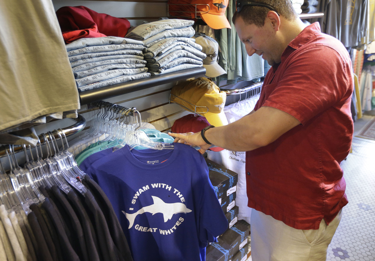 In this July 2, 2014 photo, vacationer Mark McCurdy, of Everett, Mass., examines shark-themed clothing at the Chatham Clothing Bar in Chatham, Mass. Growing sightings of great white sharks off Cape Cod are generating business for local entrepreneurs as residents and tourists seek a glimpse of the offshore predators -- or purchase their shark-themed memorabilia and apparel. (AP Photo/Steven Senne)